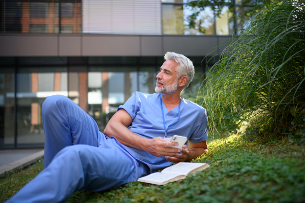 Healthcare worker resting in park outside hospital and reading book during break.