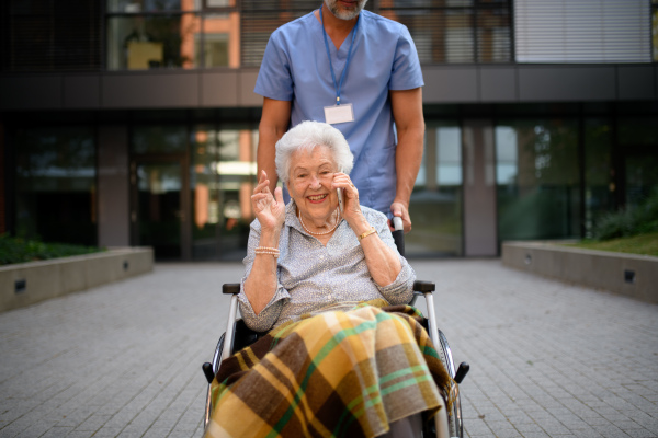 Male caregiver pushing senior woman in a wheelchair.