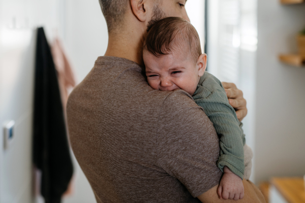 Father comforting his crying baby son, holding him in arms.