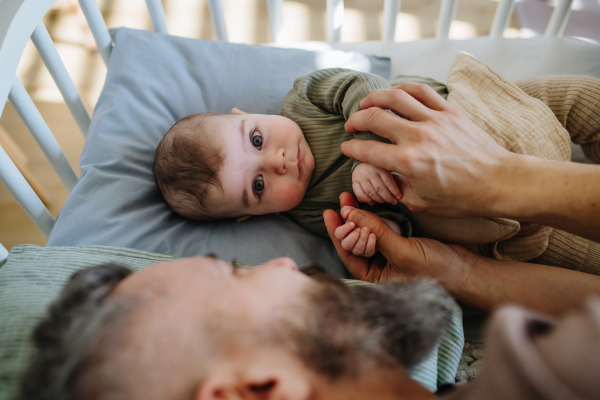 Father putting the baby to sleep, lying next to him in the crib and soothing him.