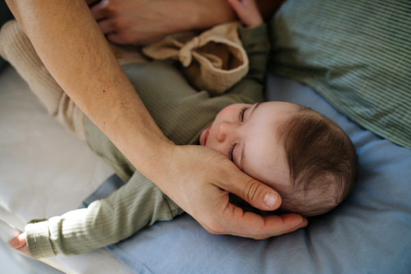 Father putting the baby to sleep, lying next to him in the crib and soothing him.