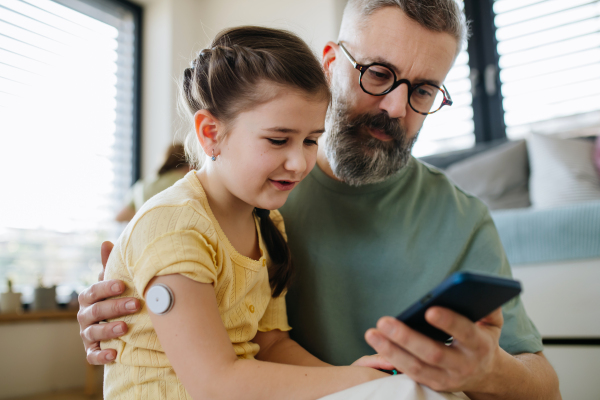 Diabetic girl with a CGM sensor on her arm. Father using an app to monitor blood sugar levels.