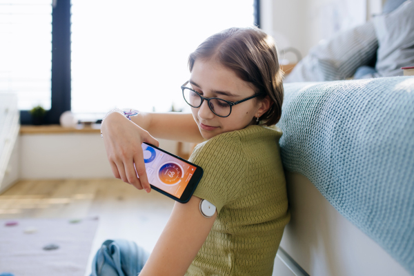 Diabetic girl with CGM sensor checking her blood sugar level in app.