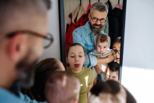 Three sisters, father and newborn brother looking in mirror. Big family concept.