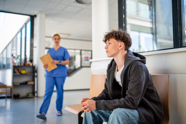 Teenage boy waiting alone in hospital waiting area before preventive medical checkup.