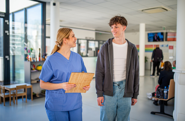 Doctor walking with teenage patient after successful checkup or medical procedure in hospital hallway.