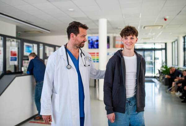 Doctor walking with teenage patient after successful checkup or medical procedure in hospital hallway.