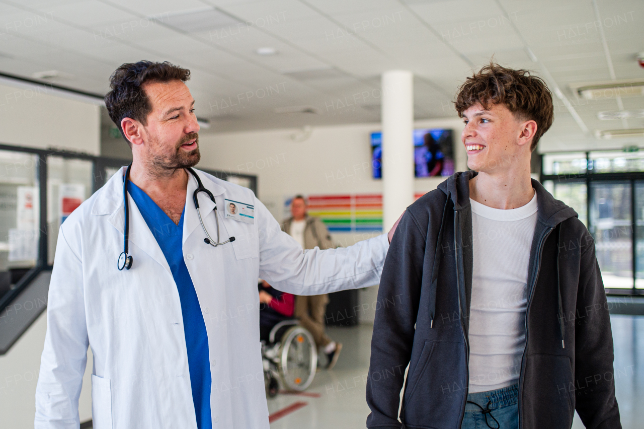 Doctor walking with teenage patient after successful checkup or medical procedure in hospital hallway.