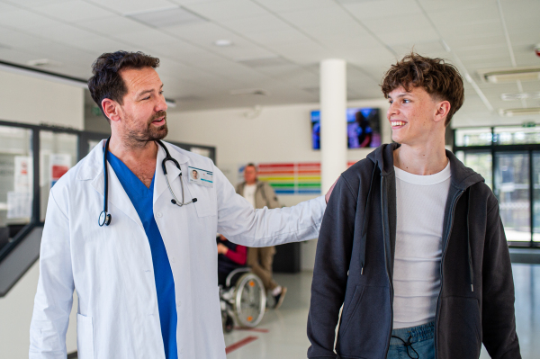 Doctor walking with teenage patient after successful checkup or medical procedure in hospital hallway.