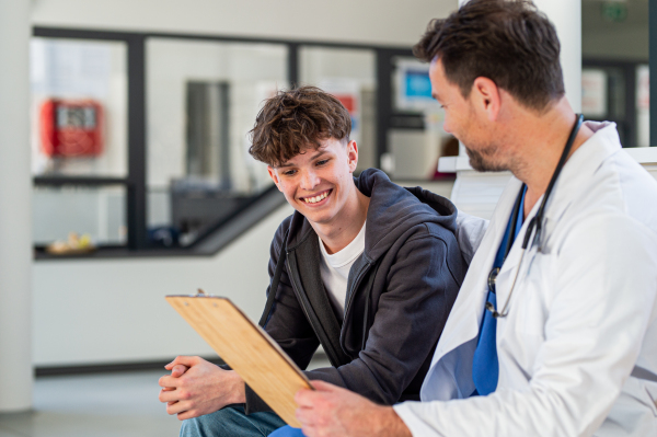 Teenage boy smiling talking with supporting doctor, receiving positive health news.