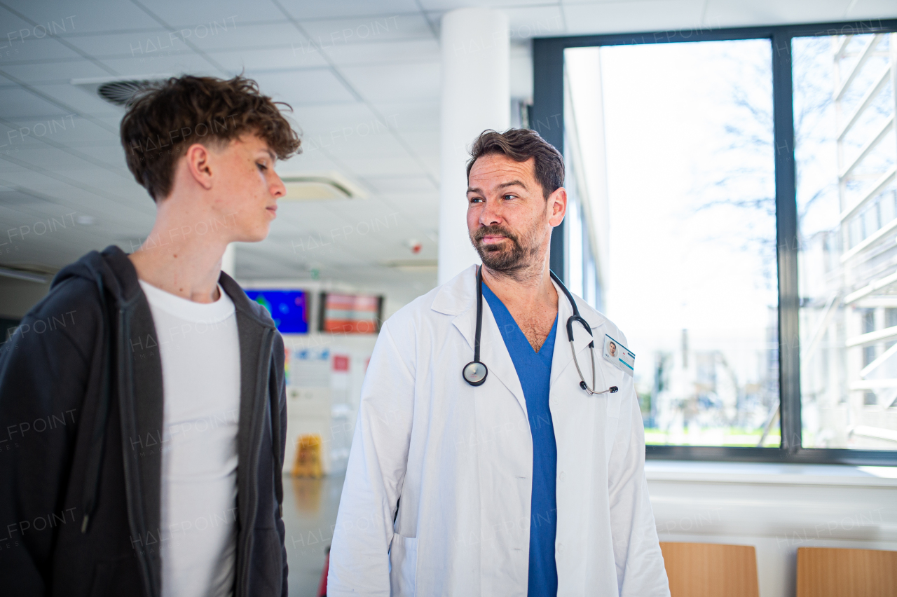 Doctor walking with teenage patient after successful checkup or medical procedure in hospital hallway.