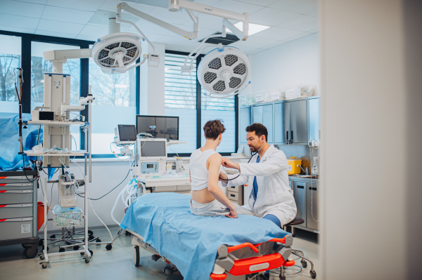Teen boy undergoing medical checkup with smiling doctor in hospital room.