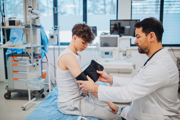 Teen boy undergoing medical checkup with smiling doctor in hospital room.