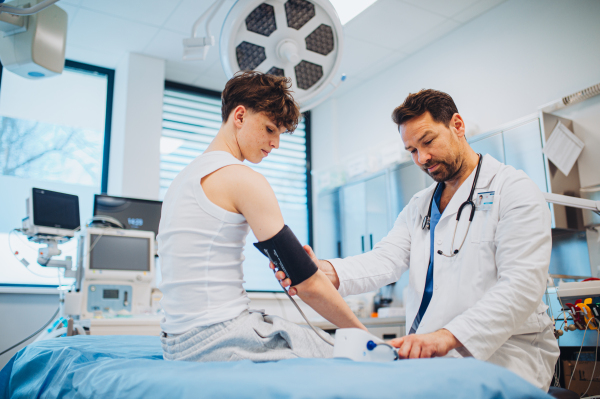 Teen boy undergoing medical checkup with smiling doctor in hospital room.