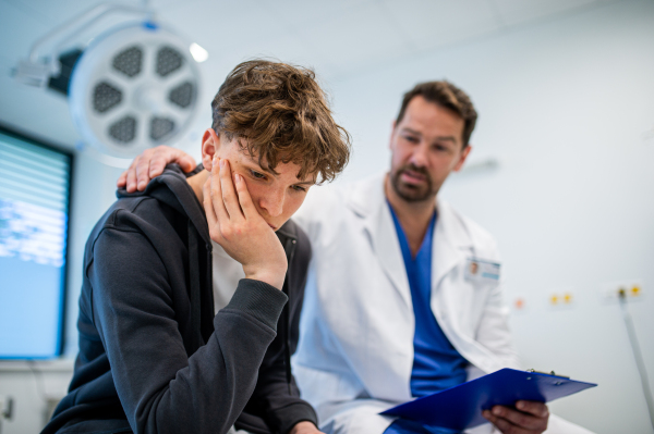 Compassionate doctor supporting anxious teenage patient before surgery. Mental health evaluation for depressed teen boy.