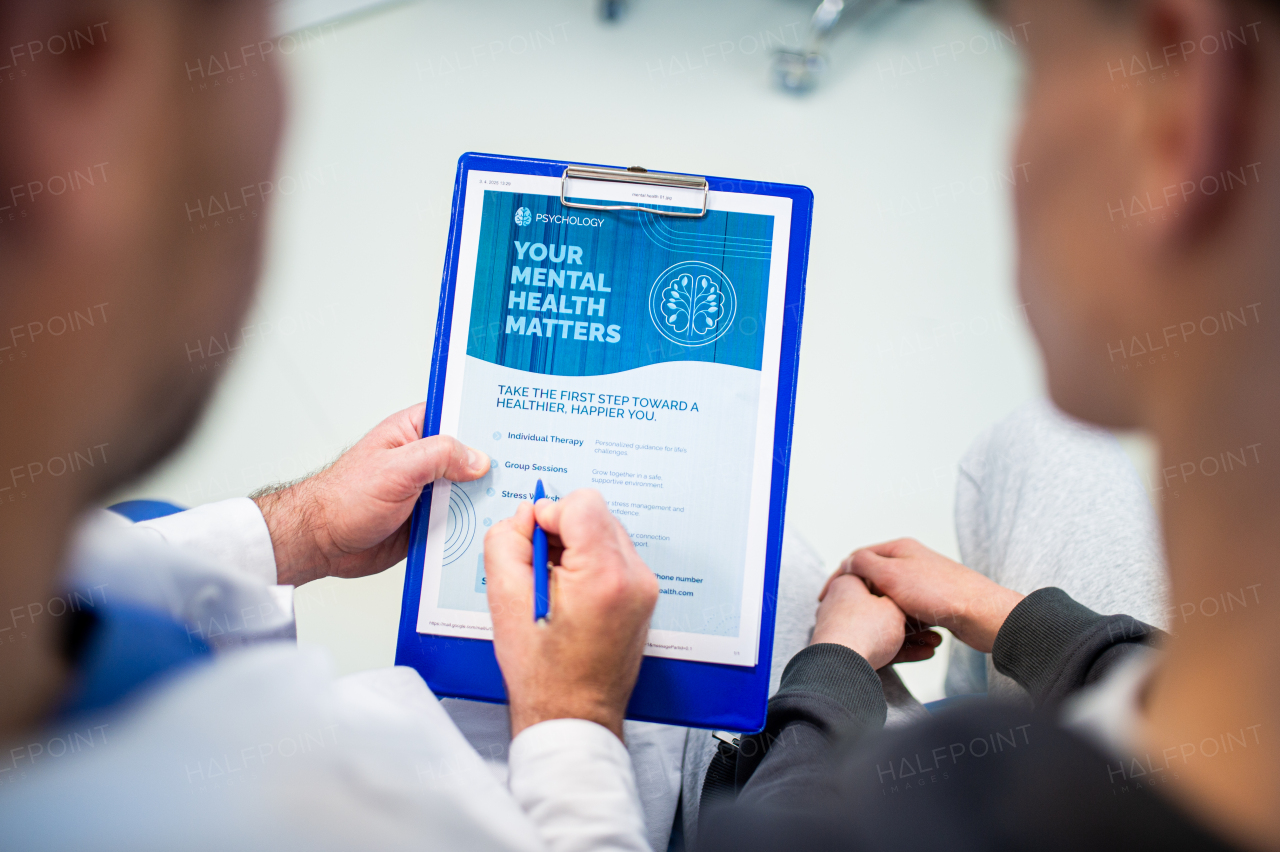 Close-up of doctor and teenage patient filling out mental health evaluation form together.