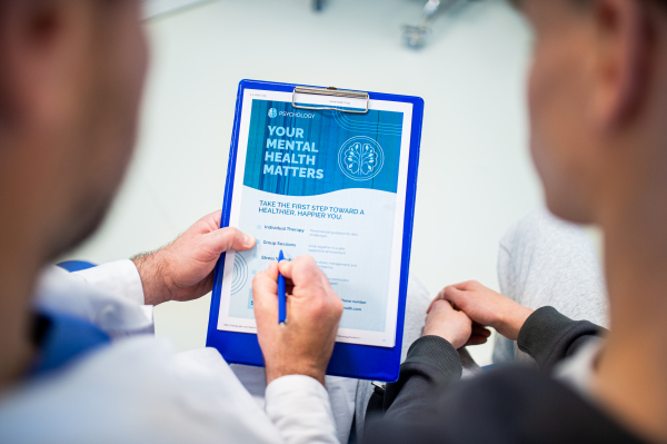 Close-up of doctor and teenage patient filling out mental health evaluation form together.