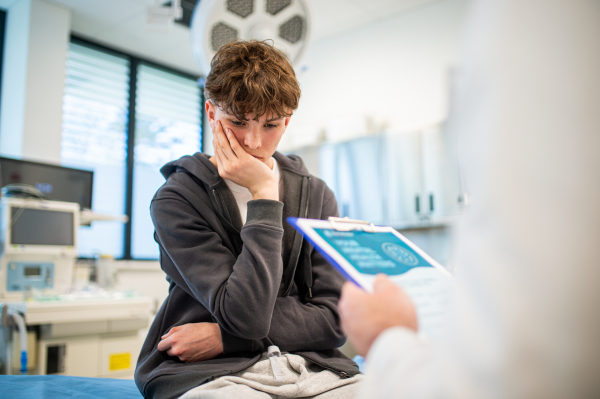 Doctor and teenage boy patient filling out mental health evaluation form together.