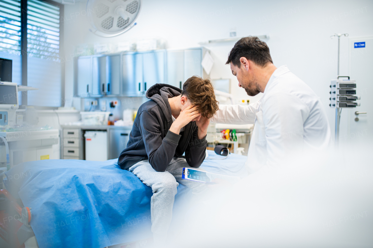 Depressed teenage boy patient sitting on hospital bed, talking with caring doctor.