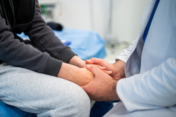 Close up of compassionate doctor holding hands of anxious teenage patient.