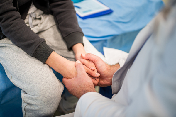 Close up of compassionate doctor holding hands of anxious teenage patient.