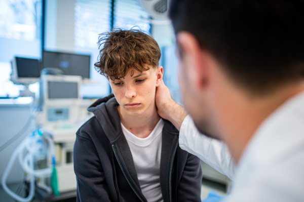 Depressed teenage boy patient sitting on hospital bed, talking with caring doctor.