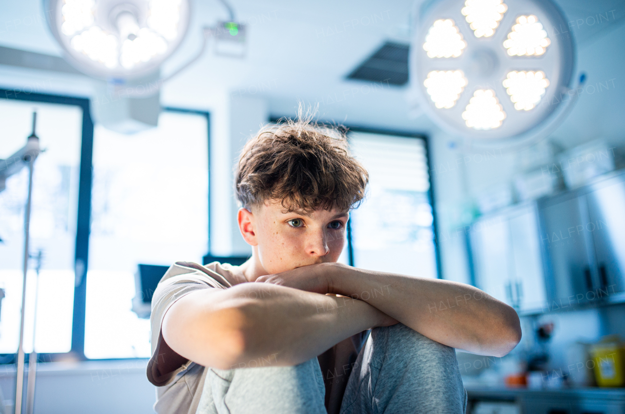 Depressed teenage boy patient sitting on hospital bed, waiting for doctor.