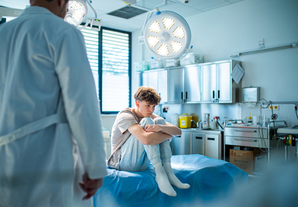Depressed teenage boy patient sitting on hospital bed, waiting for doctor.
