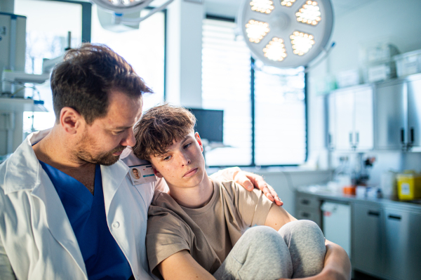 Compassionate doctor supporting anxious teenage patient before surgery. Mental health evaluation for depressed teen boy.