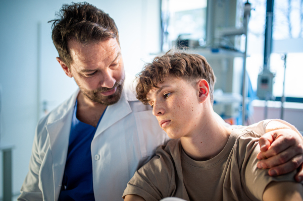 Compassionate doctor supporting anxious teenage patient before surgery. Mental health evaluation for depressed teen boy.