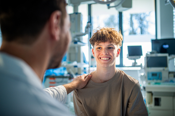 Teenage boy smiling during supportive medical consultation after receiving positive health news.