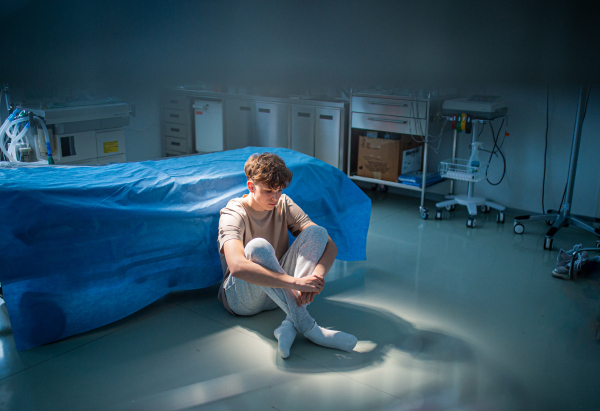 Worried teenage patient sitting alone on hospital floor, struggling with mental health issues and anxiety.