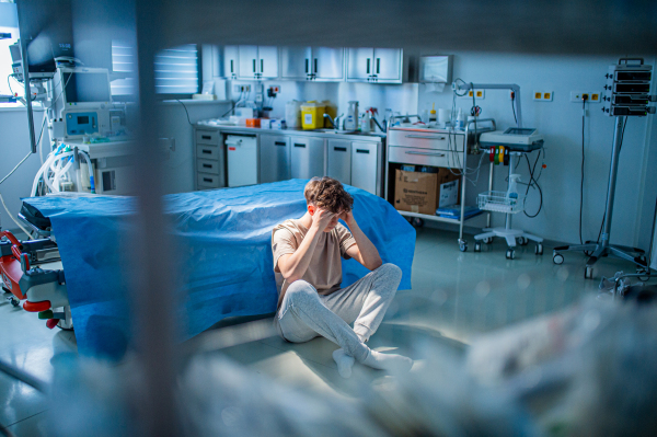 Worried teenage patient sitting alone on hospital floor, struggling with mental health issues and anxiety.