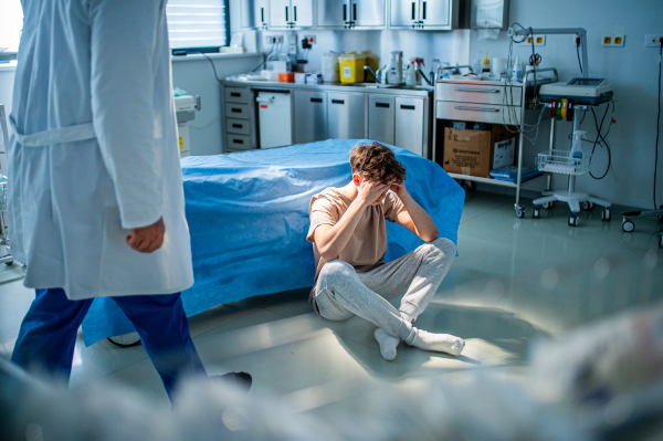 Depressed teenage boy patient sitting on hospital bed, waiting for doctor.