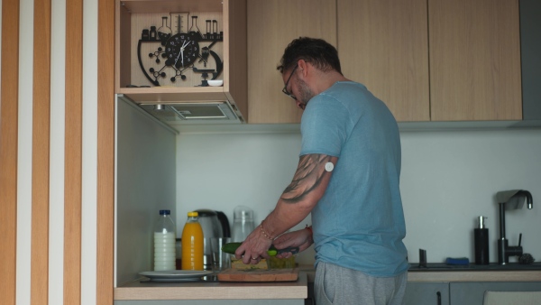 Diabetic man with CGM sensor standing in kitchen and making healthy breakfast.