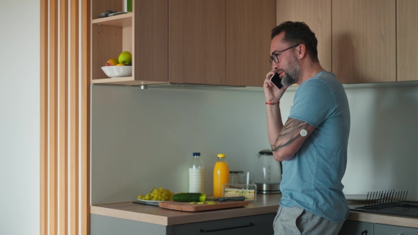 Diabetic man with CGM sensor standing in kitchen and making phone call.