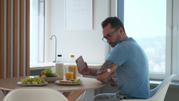 Diabetic man with CGM sensor is checking blood glucose level using smartphone app after breakfast.