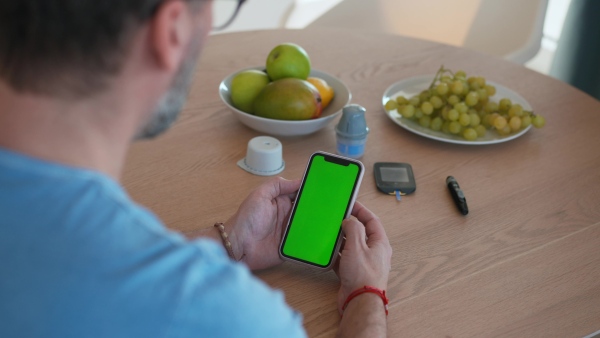 Diabetic man is checking his blood glucose level using smartphone app. Smartphone with green screen.