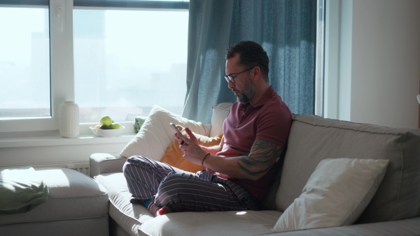 Diabetic man with CGM sensor on arm sitting on sofa and working on laptop.