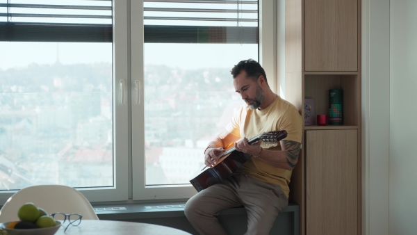Diabetic man with CGM sensor on arm playing on guitar, spending day at home.