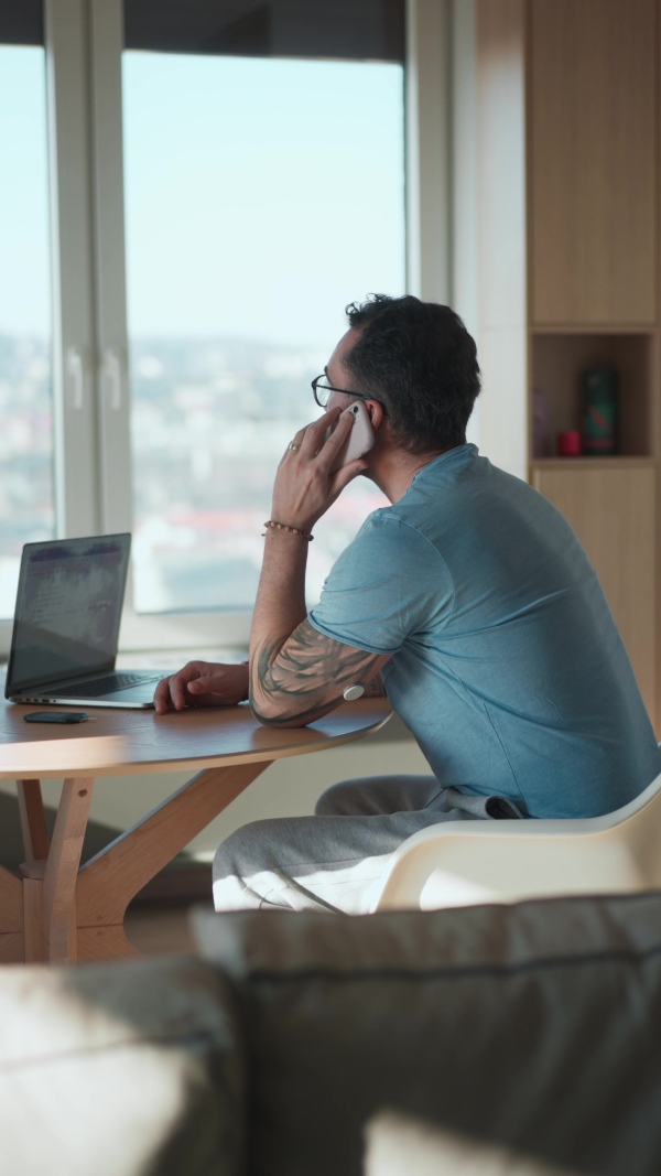 Diabetic man with CGM sensor on arm sitting at table and working on laptop and having a call.