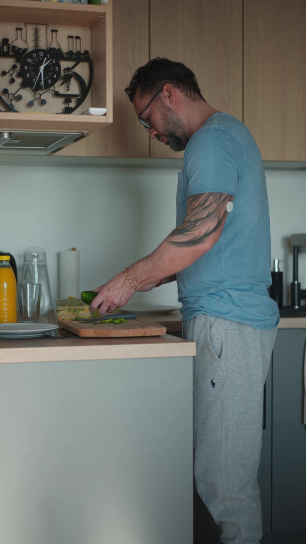 Diabetic man with CGM sensor standing in kitchen and making healthy breakfast.