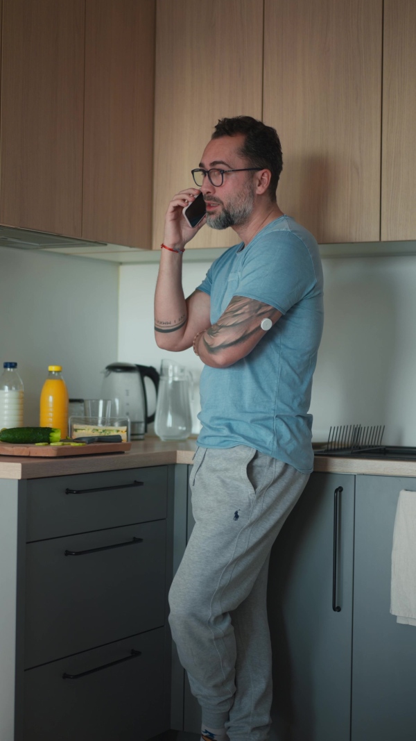 Diabetic man with CGM sensor standing in kitchen and making phone call.