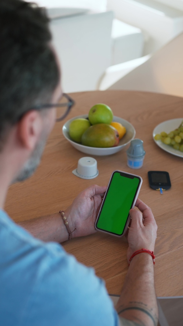 Diabetic man is checking his blood glucose level using smartphone app. Smartphone with green screen.