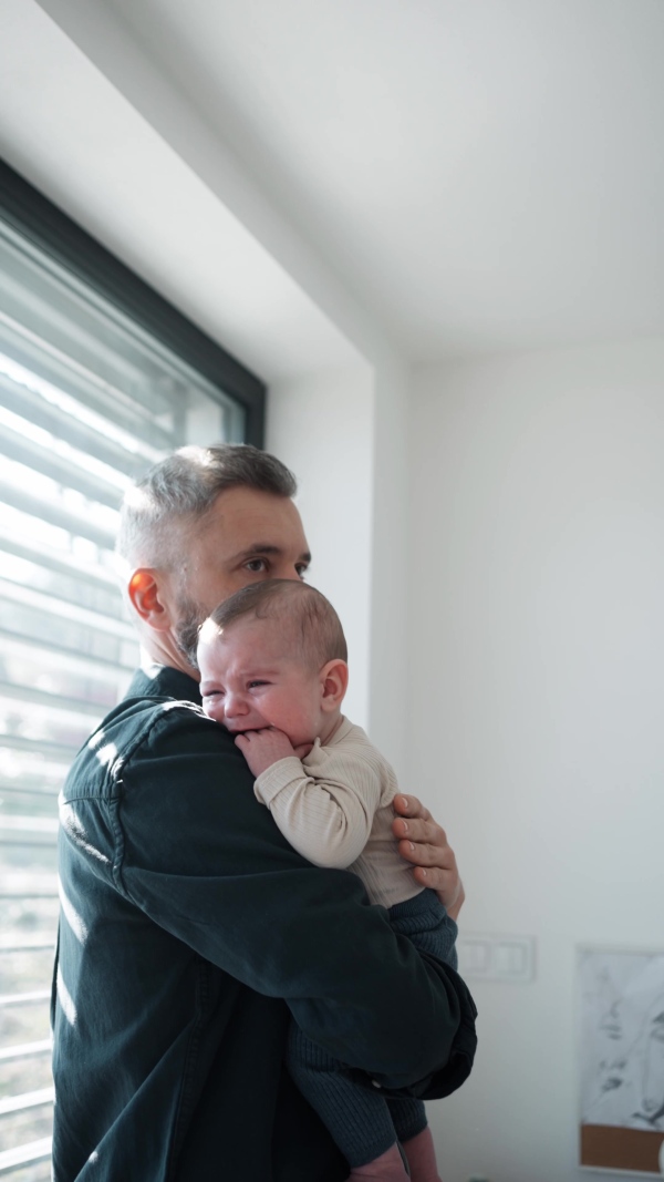 Father comforting his crying baby son, holding him in arms.