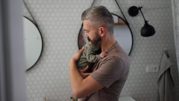 Father comforting his crying baby son, holding him in arms.