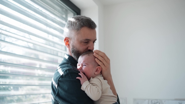 Father comforting his crying baby son, holding him in arms.