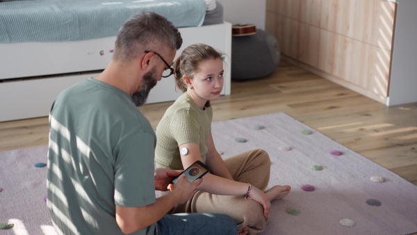 Diabetic girl with a CGM sensor on her arm. Father using an app to monitor blood sugar levels.