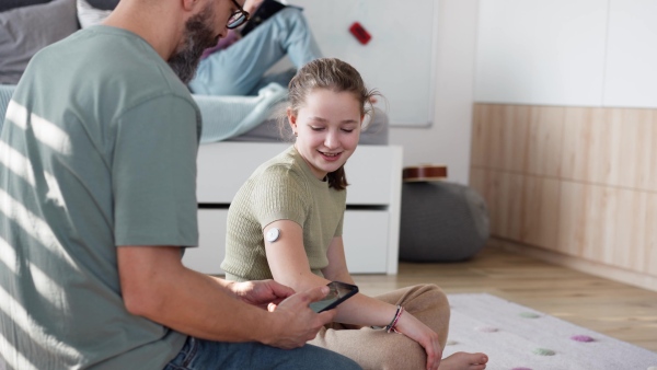 Diabetic girl with a CGM sensor on her arm. Father using an app to monitor blood sugar levels.