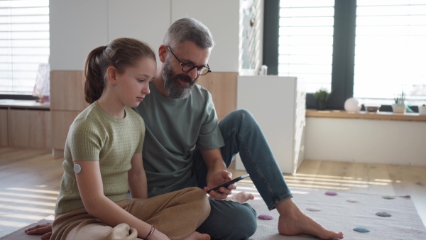 Diabetic girl with a CGM sensor on her arm. Father using an app to monitor blood sugar levels.